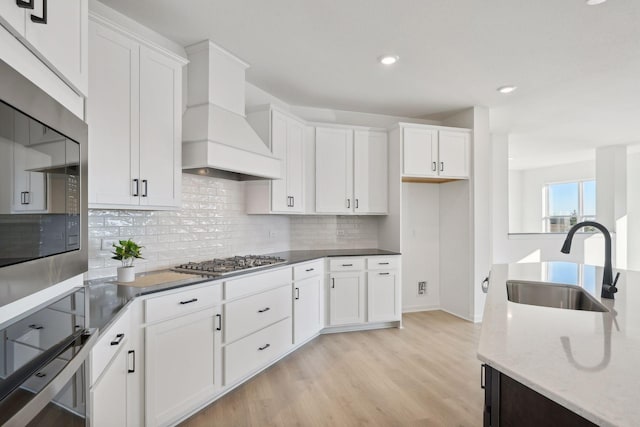 kitchen featuring stainless steel appliances, white cabinets, a sink, light stone countertops, and premium range hood