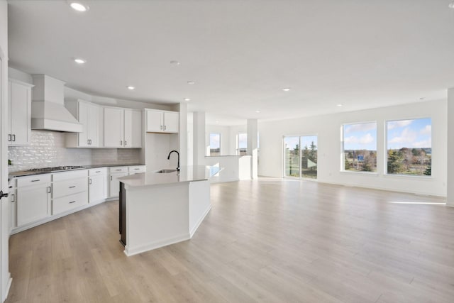 kitchen featuring tasteful backsplash, an island with sink, open floor plan, custom exhaust hood, and light wood-style floors