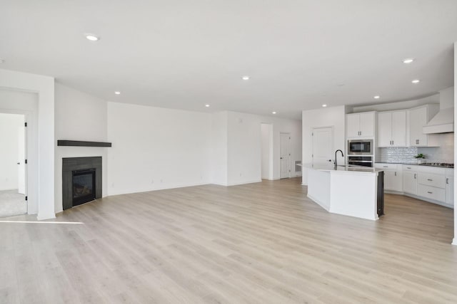 kitchen with decorative backsplash, a glass covered fireplace, open floor plan, stainless steel appliances, and white cabinetry