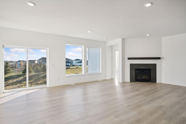 unfurnished living room with plenty of natural light, light wood-style flooring, and a glass covered fireplace