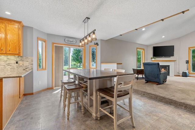 dining space featuring baseboards, vaulted ceiling, recessed lighting, a glass covered fireplace, and a textured ceiling