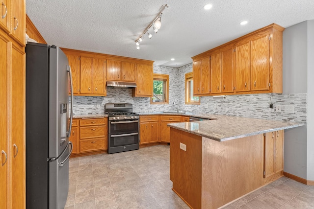 kitchen with a peninsula, a sink, stainless steel appliances, under cabinet range hood, and brown cabinets