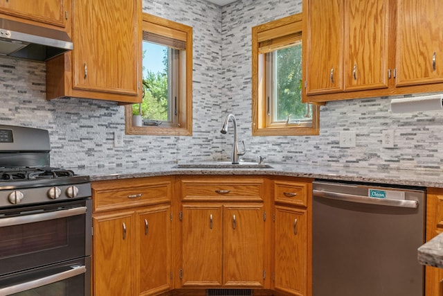 kitchen with light stone countertops, a sink, decorative backsplash, stainless steel appliances, and under cabinet range hood