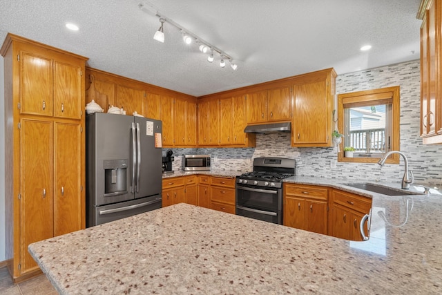 kitchen with a sink, under cabinet range hood, backsplash, stainless steel appliances, and a peninsula