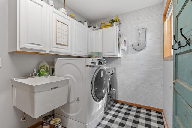 washroom with a sink, cabinet space, washing machine and dryer, and wood walls