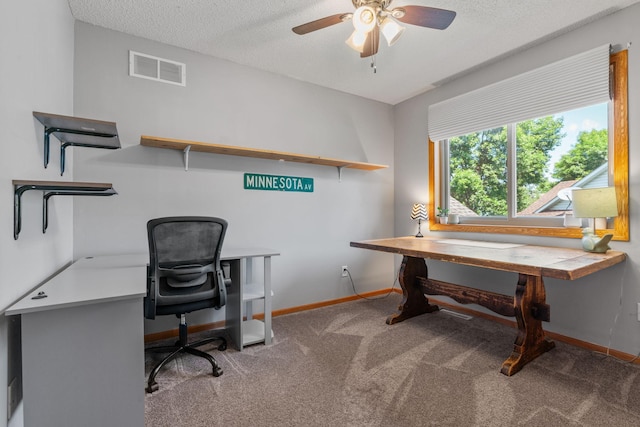 carpeted office featuring baseboards, visible vents, a textured ceiling, and a ceiling fan