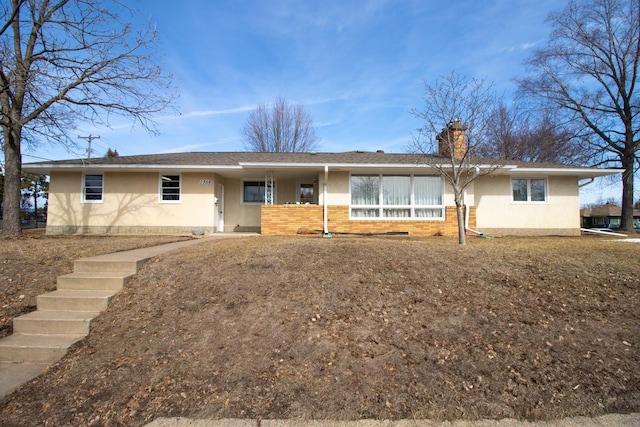 ranch-style house with stucco siding, brick siding, roof with shingles, and a chimney