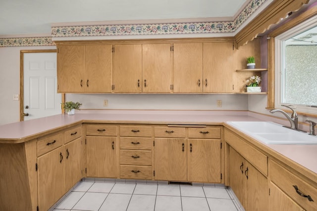 kitchen with a sink, a peninsula, light tile patterned floors, and light countertops