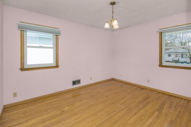 spare room with light wood-type flooring, visible vents, baseboards, and a notable chandelier