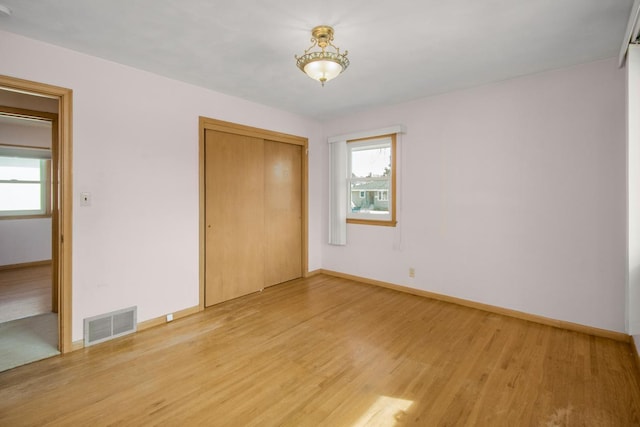 unfurnished bedroom with a closet, baseboards, visible vents, and light wood finished floors