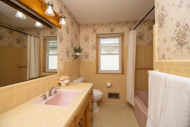 full bath with a wainscoted wall, visible vents, wallpapered walls, tile walls, and tile patterned flooring