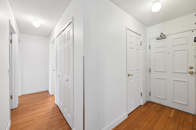 hallway featuring light wood-style flooring, a textured ceiling, and baseboards