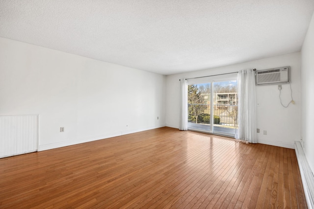 unfurnished room with a wall mounted air conditioner, baseboards, a textured ceiling, and hardwood / wood-style floors