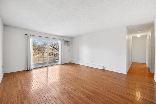 spare room with baseboards, a textured ceiling, light wood-style floors, and a wall unit AC