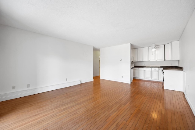 unfurnished living room with baseboards, a textured ceiling, and light wood-style flooring