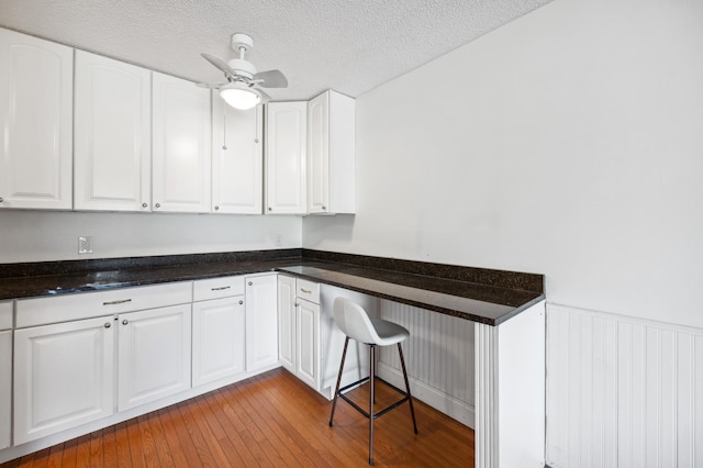 kitchen featuring a wainscoted wall, a ceiling fan, hardwood / wood-style flooring, a textured ceiling, and white cabinetry