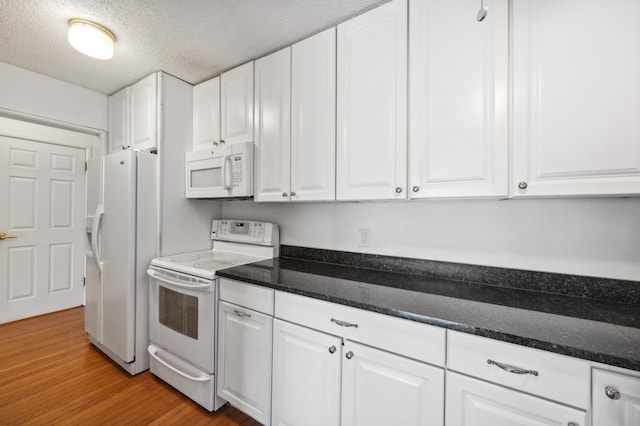 kitchen featuring dark stone counters, white appliances, white cabinetry, and light wood-style floors