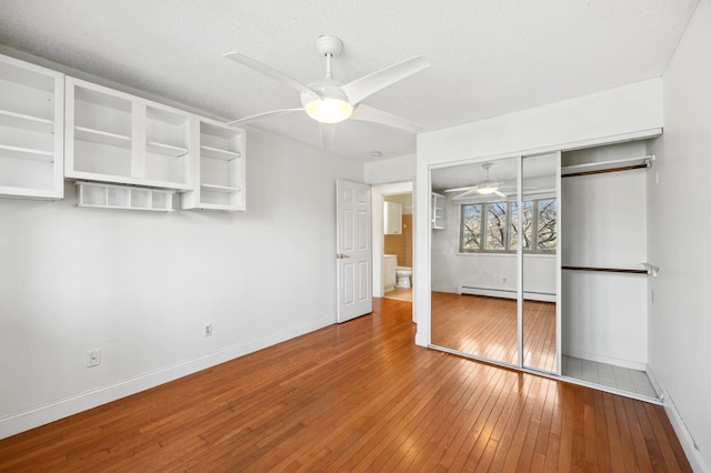 unfurnished bedroom featuring a baseboard heating unit, wood-type flooring, a textured ceiling, and baseboards