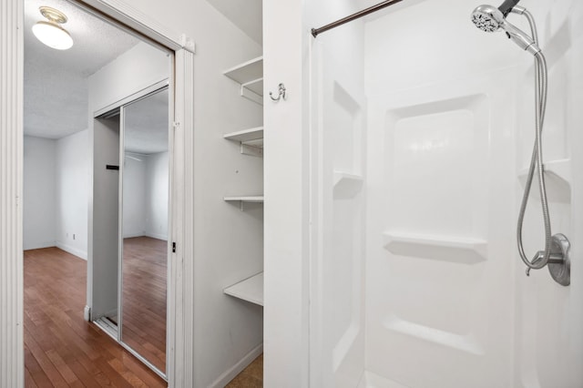 full bathroom featuring baseboards, a textured ceiling, walk in shower, and wood-type flooring