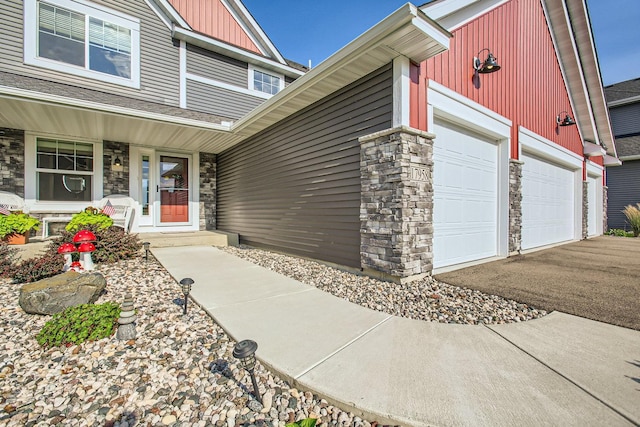 view of exterior entry with a garage, stone siding, aphalt driveway, and board and batten siding