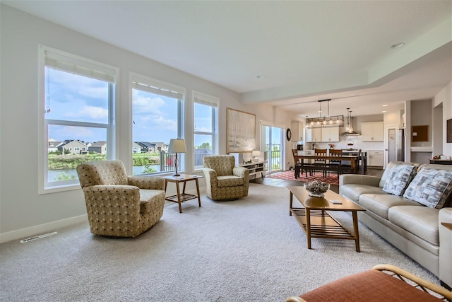 carpeted living area featuring an inviting chandelier, baseboards, and visible vents