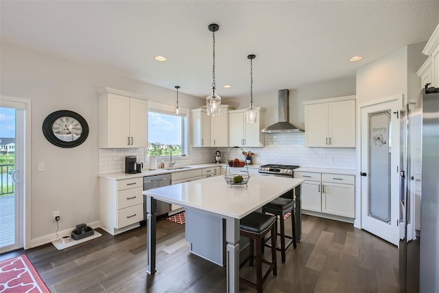 kitchen with wall chimney exhaust hood, a breakfast bar area, a sink, stainless steel appliances, and backsplash