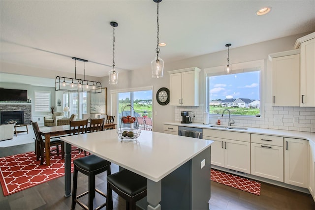 kitchen with a stone fireplace, a sink, light countertops, backsplash, and a center island