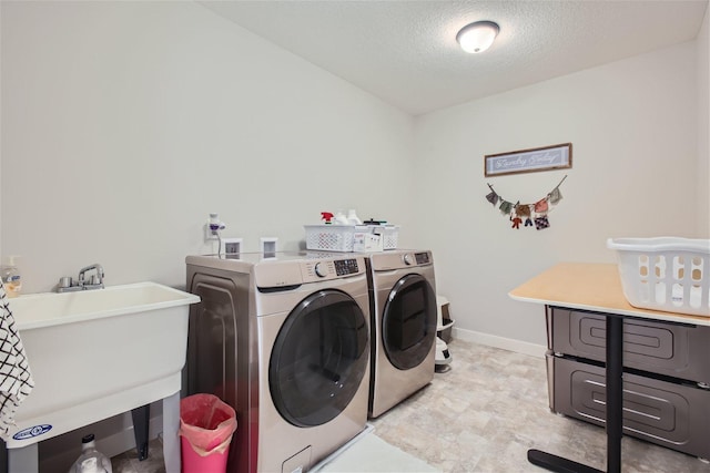 laundry room with a textured ceiling, laundry area, a sink, baseboards, and washing machine and clothes dryer