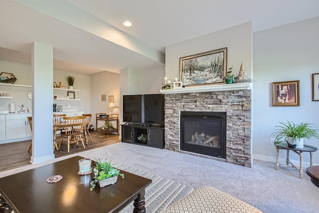 carpeted living area with recessed lighting, baseboards, a sink, and a stone fireplace