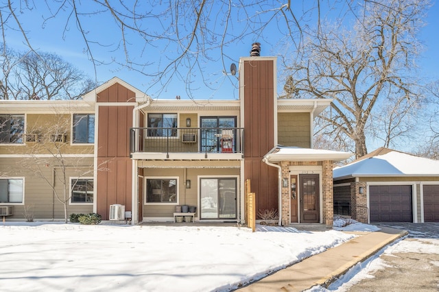 view of front of house with a balcony, an attached garage, a chimney, board and batten siding, and brick siding