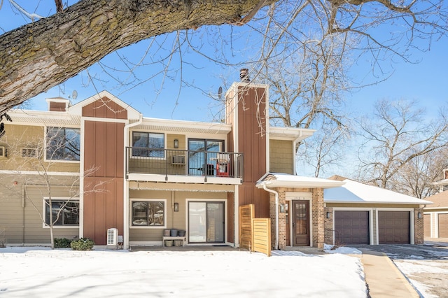 view of front of property with brick siding, board and batten siding, a chimney, a balcony, and an attached garage