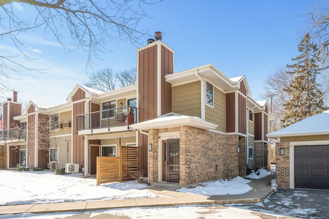 multi unit property with a balcony, board and batten siding, an outdoor structure, a garage, and brick siding