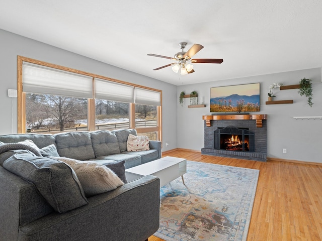 living room featuring a brick fireplace, a ceiling fan, baseboards, and wood finished floors