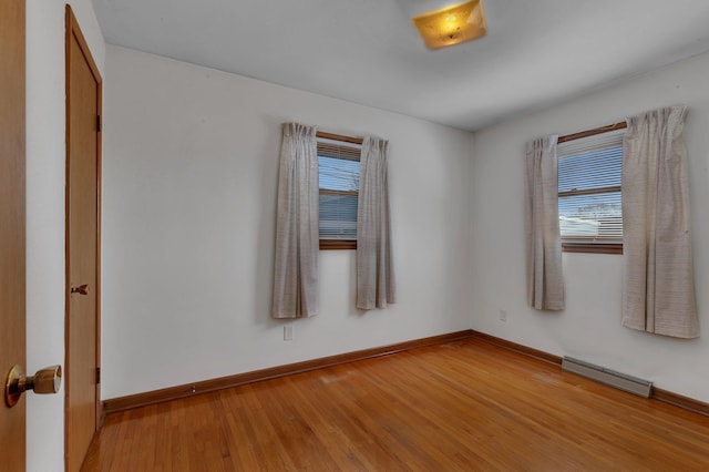 spare room featuring a baseboard heating unit, wood finished floors, and baseboards