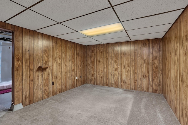 unfurnished room featuring a drop ceiling, wood walls, and carpet