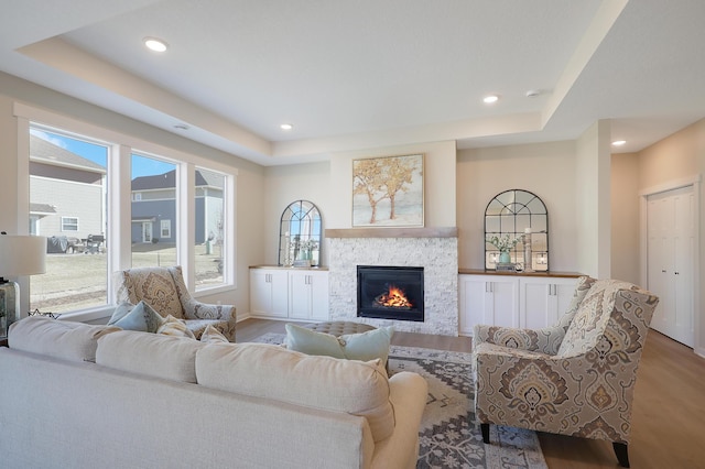 living room featuring light wood finished floors, baseboards, a raised ceiling, a glass covered fireplace, and recessed lighting