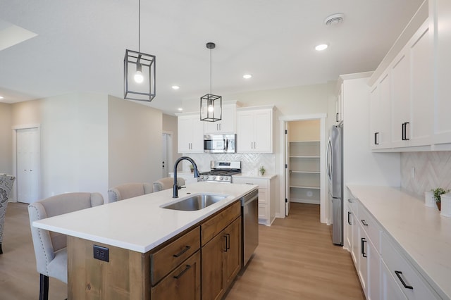 kitchen featuring an island with sink, a kitchen breakfast bar, stainless steel appliances, white cabinetry, and a sink