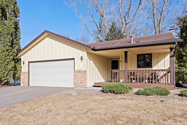 ranch-style house with brick siding, a porch, a chimney, driveway, and an attached garage