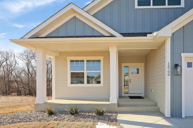 view of exterior entry featuring covered porch, a shingled roof, and board and batten siding