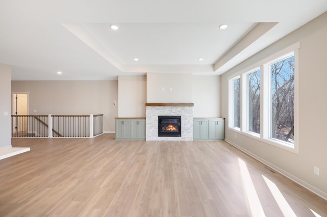 unfurnished living room with light wood-style floors, recessed lighting, a raised ceiling, and baseboards