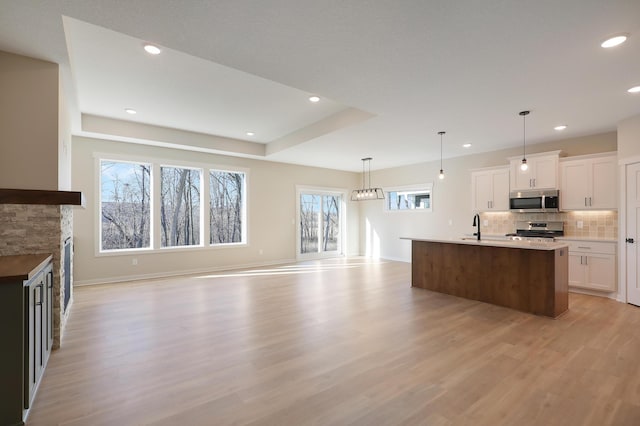 kitchen with stainless steel appliances, backsplash, open floor plan, a sink, and light wood-type flooring