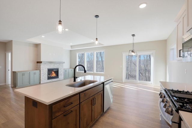 kitchen with light countertops, appliances with stainless steel finishes, open floor plan, a sink, and a stone fireplace