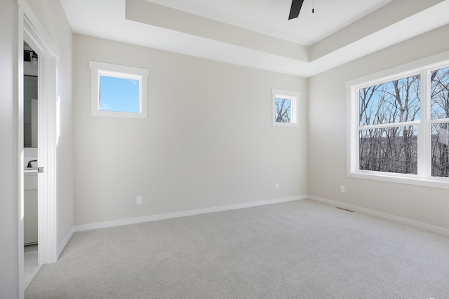 unfurnished bedroom with light carpet, visible vents, baseboards, a raised ceiling, and a ceiling fan