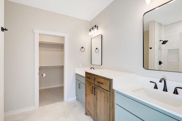 bathroom with two vanities, a spacious closet, a sink, a tile shower, and baseboards