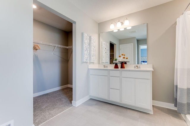 full bath with a spacious closet, visible vents, baseboards, double vanity, and a sink