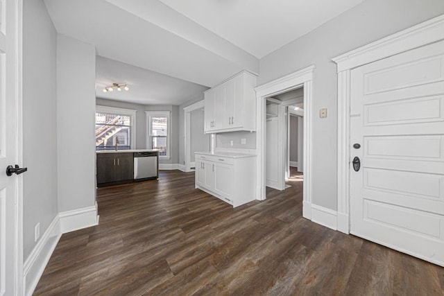 kitchen featuring dark wood-style flooring, light countertops, stainless steel dishwasher, white cabinetry, and baseboards