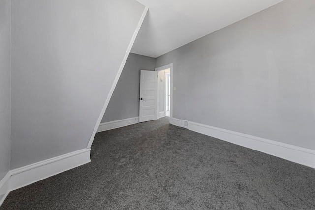 spare room featuring dark colored carpet and baseboards