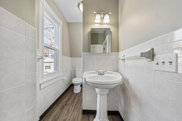 half bath with toilet, wainscoting, wood finished floors, and tile walls