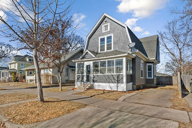 view of front of home featuring entry steps, fence, a sunroom, a gambrel roof, and roof with shingles