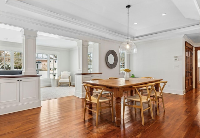 dining room with a raised ceiling, decorative columns, wood finished floors, and ornamental molding